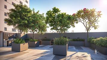 Un jardín en la azotea con plantas en macetas, mobiliario exterior y vistas a la ciudad.