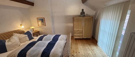 A bedroom with a bed, wooden floor, a cabinet, and a window with blinds.