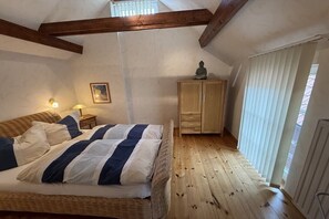 Une chambre à coucher avec un lit, un plancher en bois, une armoire et une fenêtre avec des stores.