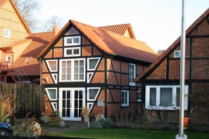 Une maison traditionnelle à colombages, dotée d’un toit à forte pente, de nombreuses fenêtres et d’un jardin bien entretenu.
