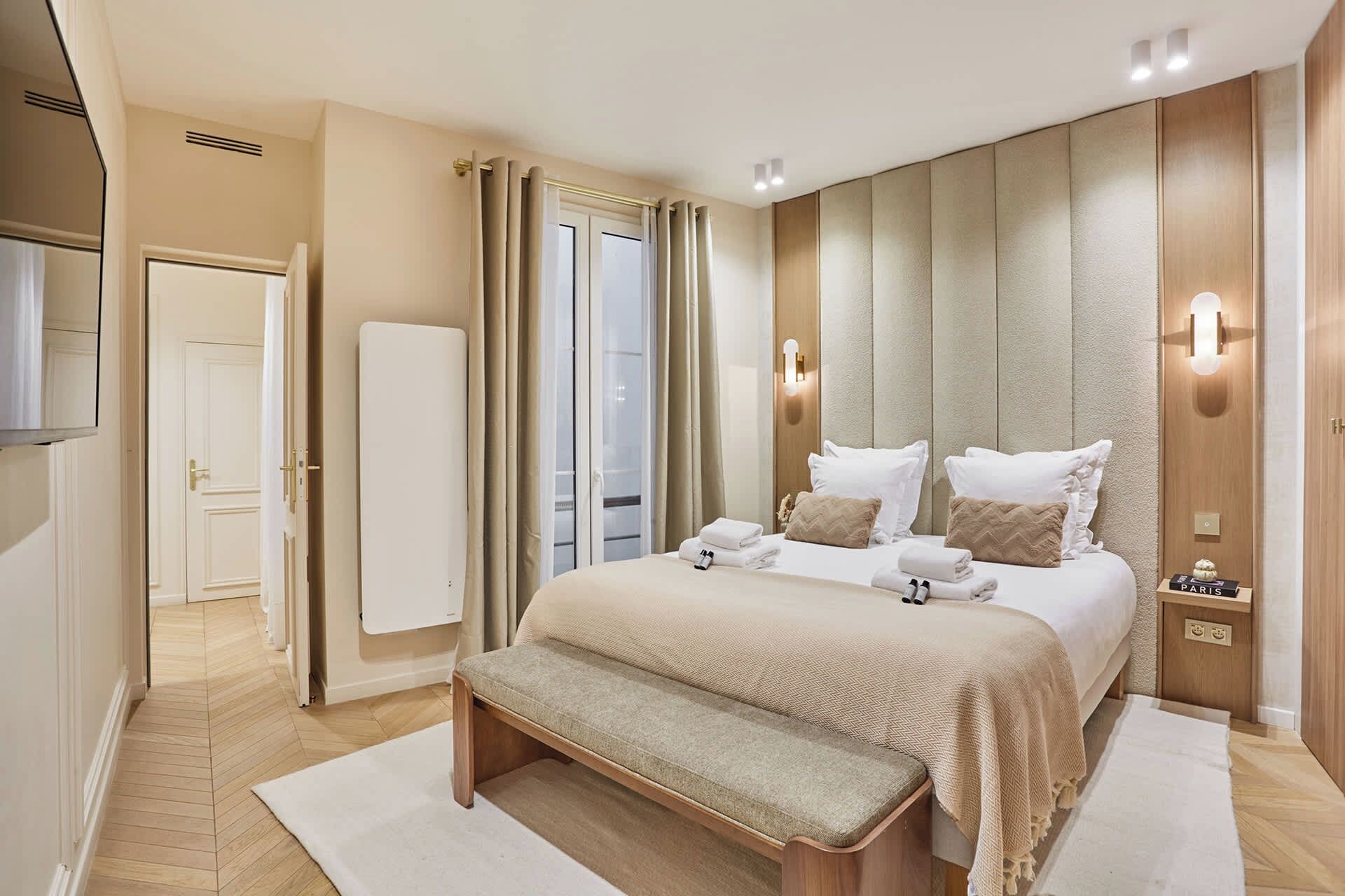 Une chambre d’hôtel moderne avec un grand lit, un banc, une armoire et une vue sur l’extérieur.