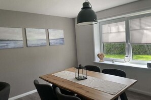 A dining area with a wooden table, four chairs, a pendant light, and three paintings on the wall. - Holiday apartment with 2 bedrooms (Kappeln)