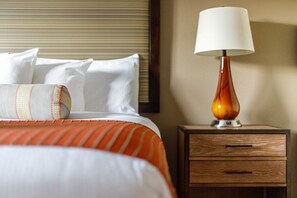 A hotel room with a bed, pillows, a striped blanket, a nightstand with a lamp, and a drawer. - Lincoln NH | Ski Retreat | Pool, Near Loon & Hiking Trails (Lincoln)