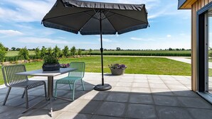 Een terras buiten met een tafel, stoelen, een grote parasol en potplanten.