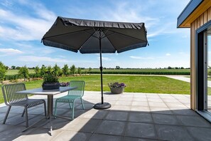 An outdoor patio with a table and chairs, a large umbrella, and potted plants. - Holiday home with 1 bedroom (Zonnemaire)