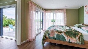 Een slaapkamer met een bed, gordijnen en een uitzicht door de glazen deur.