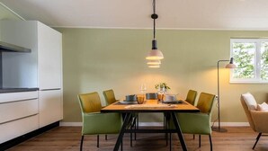 Een eethoek met een tafel voor vier personen, omringd door groene stoelen, een hanglamp erboven en een raam met uitzicht.