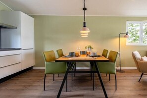 A dining area with a table set for four, surrounded by green chairs, a pendant light above, and a window with a view. - Holiday home with 1 bedroom (Zonnemaire)