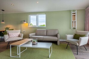 Un salon avec un canapé, des fauteuils, une table basse, une lampe et une fenêtre.