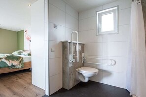 A compact bathroom with a toilet, a shower area, and a window. - Holiday home with 1 bedroom (Zonnemaire)