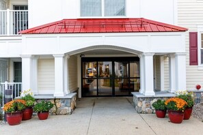 Un ingresso di un edificio con tetto rosso, colonne bianche e piante in vaso.