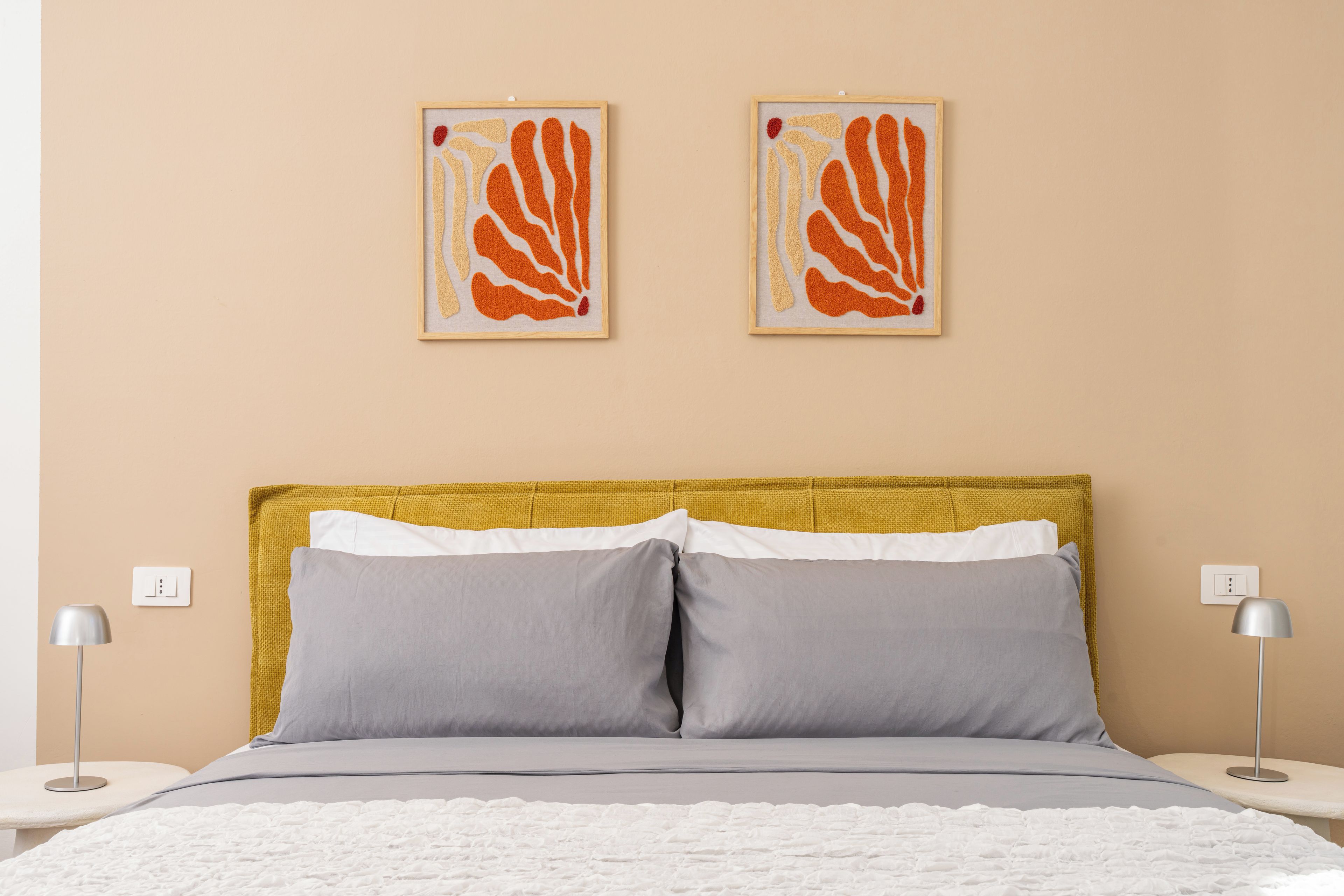 A bed with a white textured blanket, two gray pillows, and a yellow headboard.