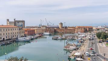 A marina with boats docked, a historic fort, and a busy street with cars and a café.
