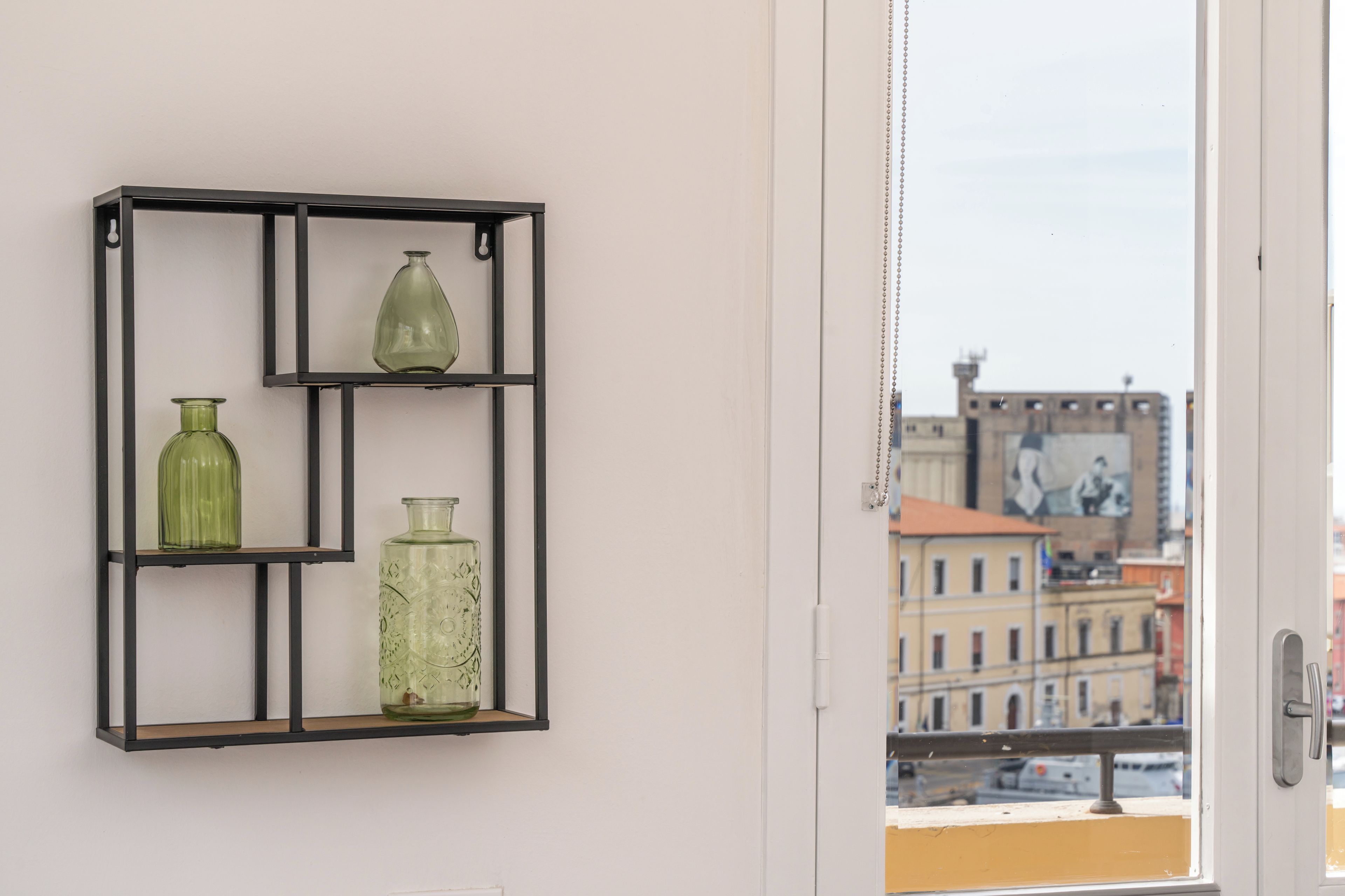A room with a black metal shelf holding three glass vases.