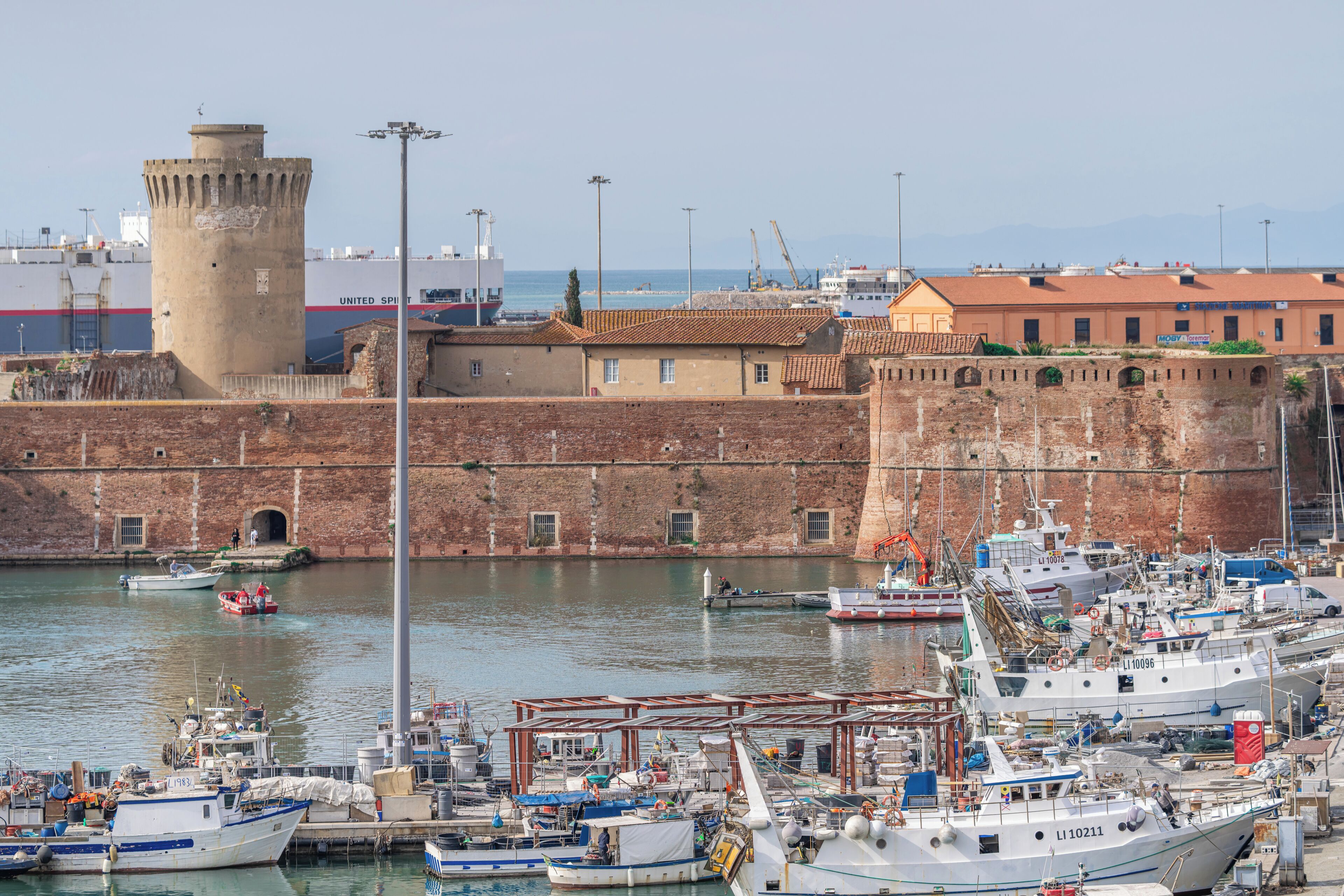 A harbor with boats docked, a historic fort, and a building with a red roof.