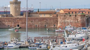 A harbor with boats docked, a historic fort, and a building with a red roof. - Porto Mediceo (Livorno)