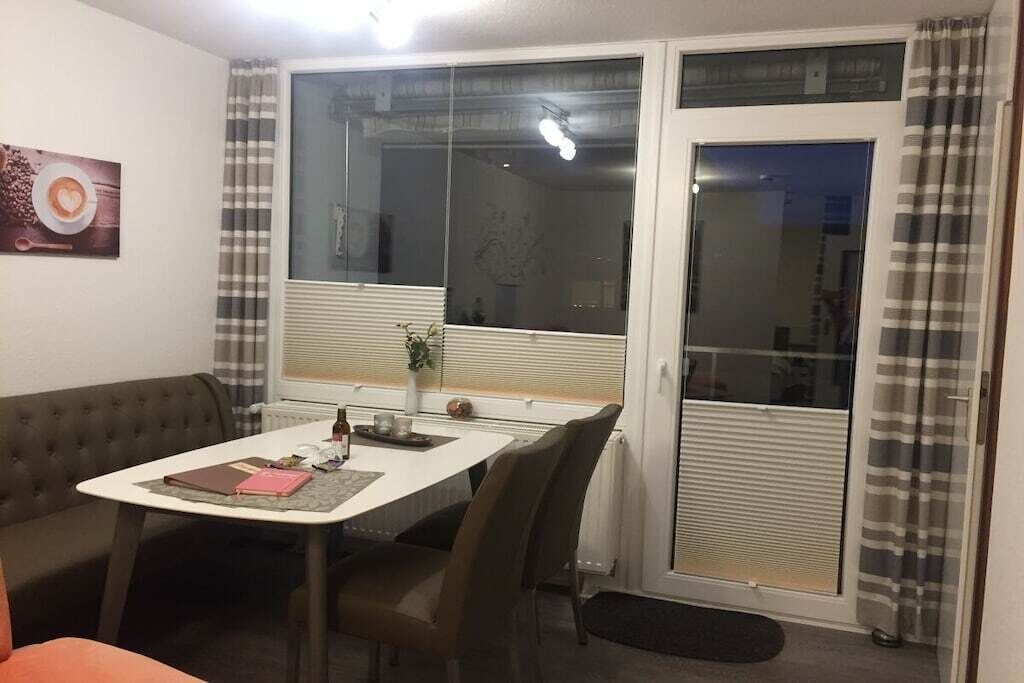 Un comedor con una mesa, sillas, un banco y una ventana con cortinas.