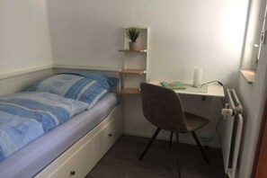 A small, compact room with a single bed, a desk with a chair, a radiator, and a shelf with a plant. - Holiday apartment with 2 bedrooms (Altenau)