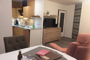 A compact living space with a kitchenette, a dining area with a table and chairs, and a television in the living area. - Holiday apartment with 2 bedrooms (Altenau)