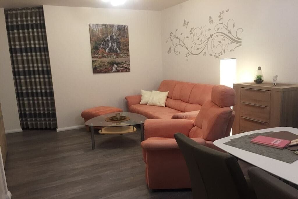 Un salon comprenant un canapé, une table basse, une table à manger avec des chaises, une lampe et un élément de décoration murale.