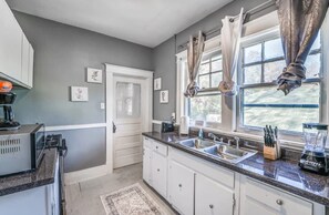 Eine Küche mit weißen Schränken, einer Granit Arbeitsplatte, einer Spüle und einem Fenster mit Vorhängen.