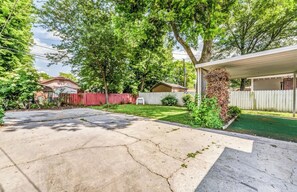 A residential backyard with a paved driveway, a covered patio area, a fenced yard, and mature trees. - Near Shopping & Dining- Magic in Midtown- Unit A (Memphis)