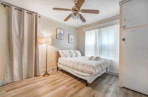 A bedroom with a bed, a floor lamp, a ceiling fan, and a window with curtains. - Near Shopping & Dining- Magic in Midtown- Unit B (Memphis)