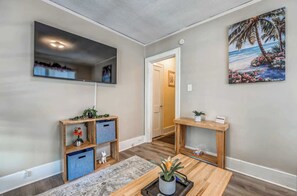 A room with a flat-screen TV mounted on the wall, a wooden console table with a plant, and a door leading to another room. - Near Shopping & Dining- Magic in Midtown- Unit B (Memphis)