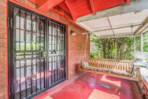 A covered porch with a swing seat, a black gate, and a brick wall. - Near Shopping & Dining- Magic in Midtown- Unit B (Memphis)