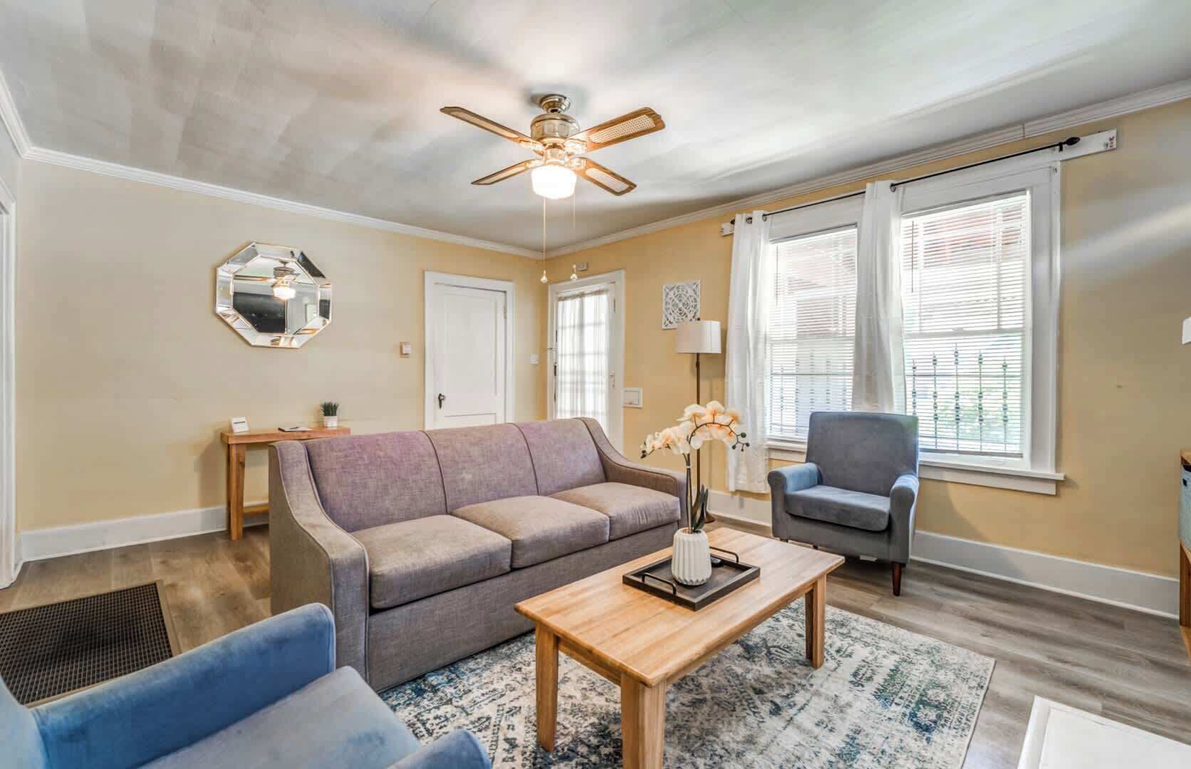 A living room with a sofa, armchair, coffee table, and a ceiling fan.