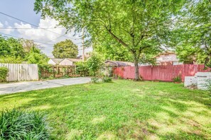 A residential backyard with a grassy lawn, a wooden fence, and a house in the background. - Near Shopping & Dining- Magic in Midtown- 2 Units (Memphis)