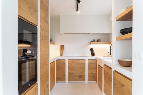 Een moderne keuken met houten kastjes, een inbouwoven en een aanrecht met diverse spullen.