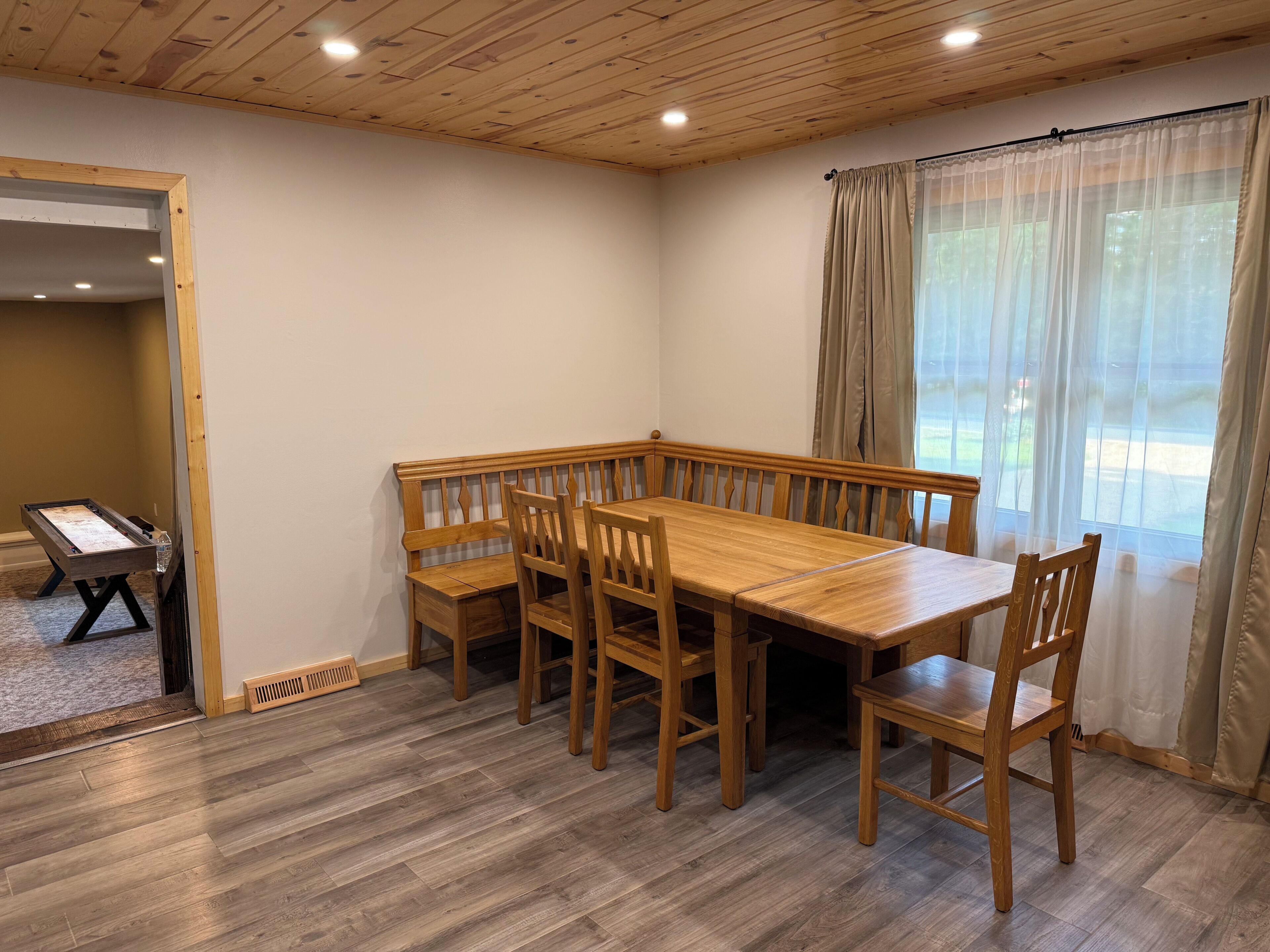A dining area with a wooden table and benches, a window with curtains, and a view of the outdoors.