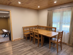 Een eetruimte met een houten tafel en banken, een raam met gordijnen en uitzicht op de omgeving.