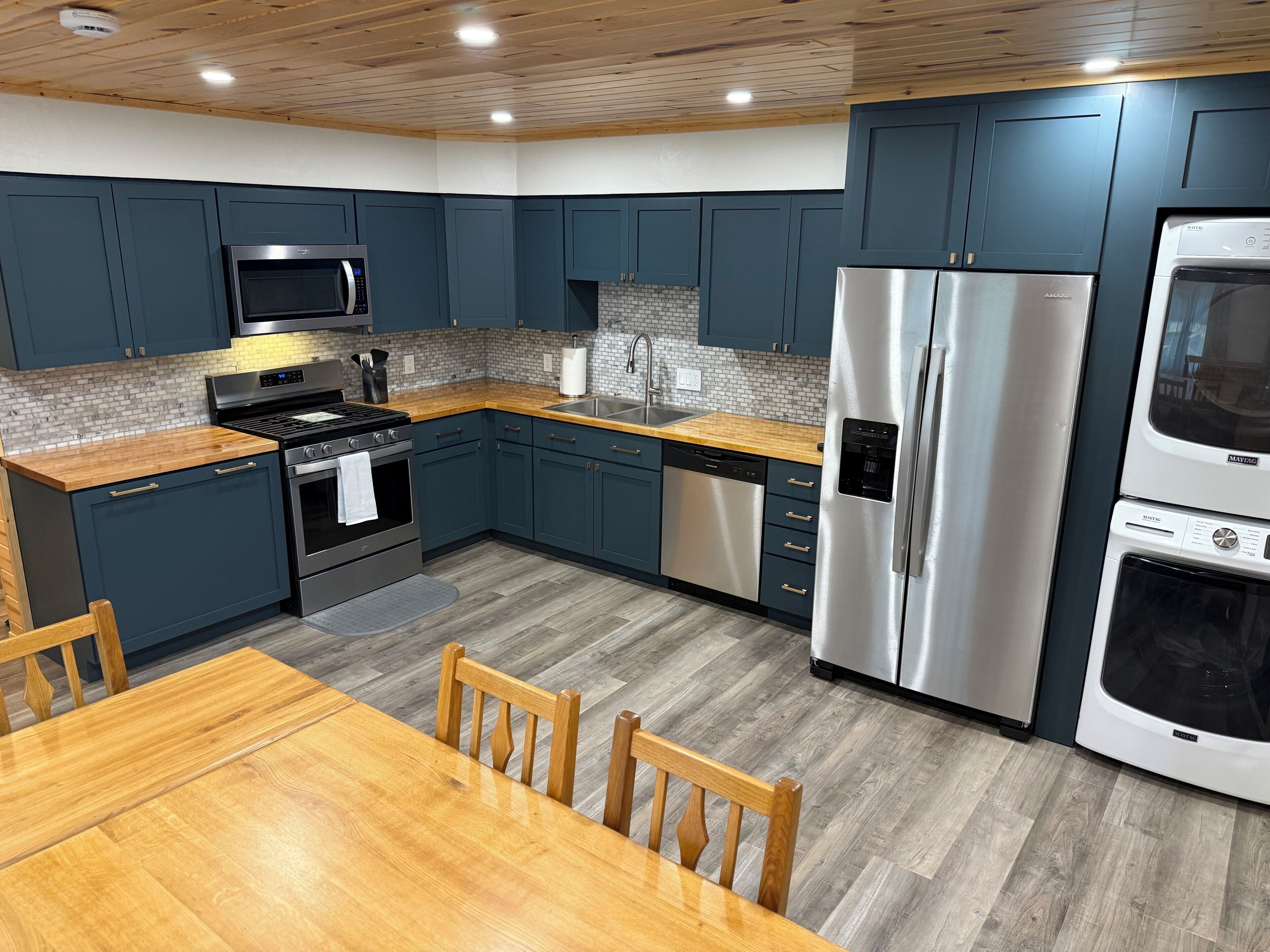 A modern kitchen with dark blue cabinets, stainless steel appliances, a wooden countertop, and a dining table with chairs.