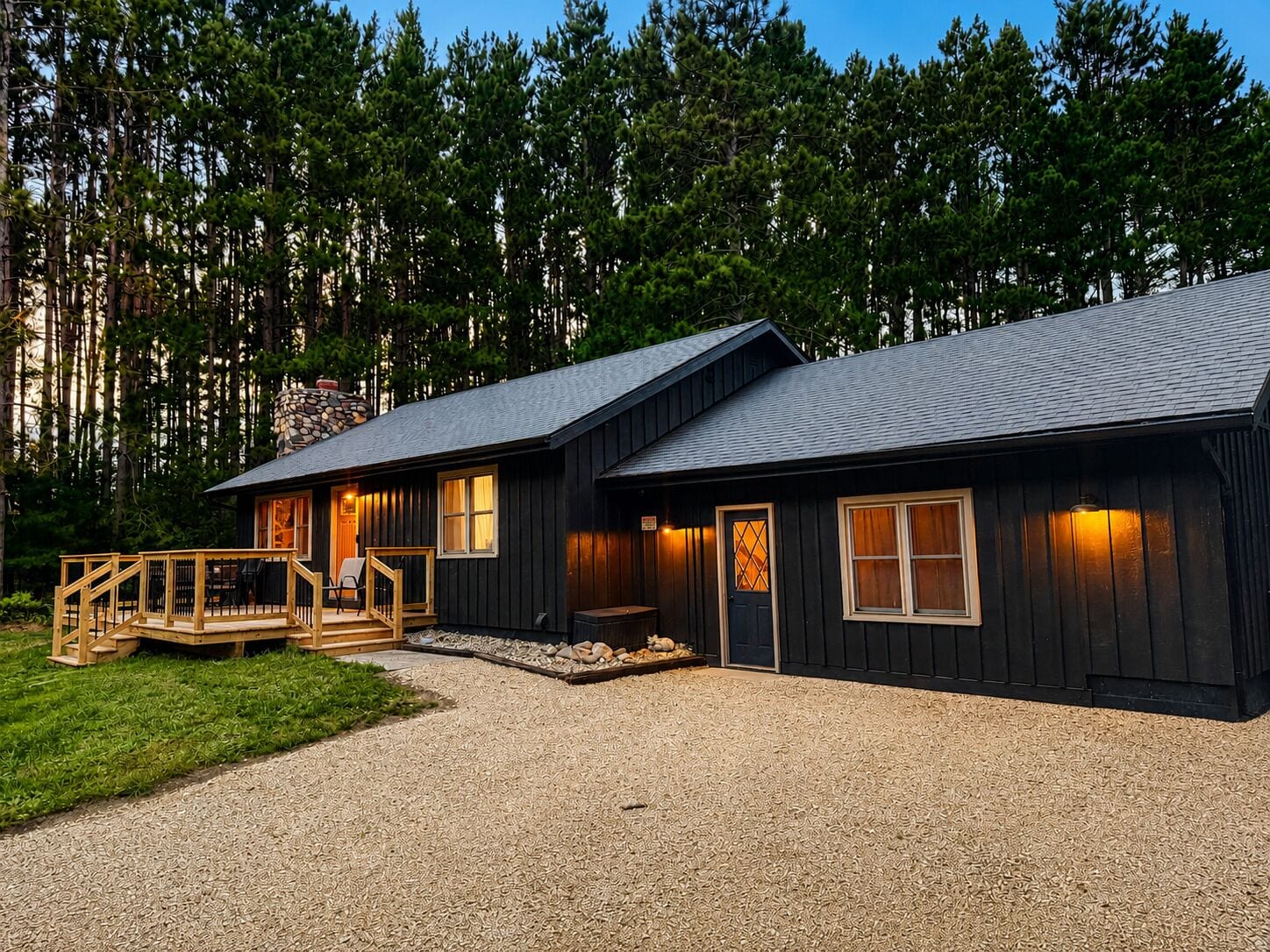 A two-story cabin with a porch, surrounded by a forest.