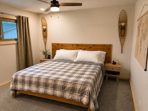 Een slaapkamer met een houten bed, een nachtkastje, een plafondventilator en een raam met gordijnen.