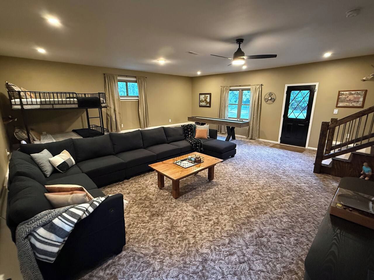 A living room with a sectional sofa, a coffee table, a bunk bed, and a staircase.