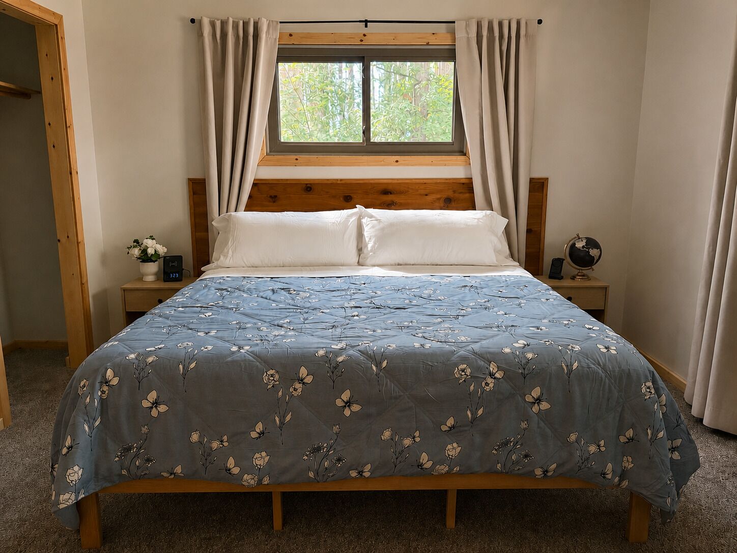 Une chambre à coucher avec un lit en bois, une fenêtre avec des rideaux, une table de chevet avec un globe terrestre et une plante, et une petite table de nuit avec une horloge.