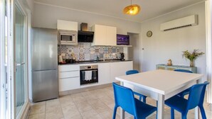 A modern kitchen with a stainless steel refrigerator, microwave, and oven, a tiled backsplash, and a dining area with a white table and blue chairs. - Calabria – Vacation Home with a Garden, Ocean View, and Close to the Beach Near Tropea and Pizzo (Località Punta Safò Briatico)