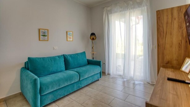 A room with a teal sofa, a wooden desk, and a large window with sheer curtains. - Calabria – Vacation Home with a Garden, Ocean View, and Close to the Beach Near Tropea and Pizzo (Località Punta Safò Briatico)