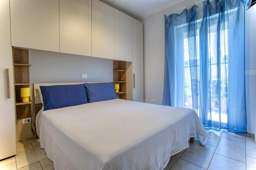 Une chambre à coucher avec un lit, des étagères intégrées et une fenêtre ornée de rideaux légers.