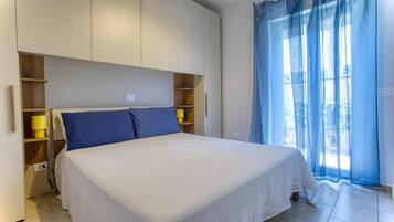 Une chambre à coucher avec un lit, des étagères intégrées et une fenêtre ornée de rideaux légers.