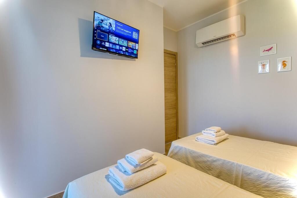Ein Hotelzimmer mit zwei Betten, einem an der Wand befestigten Fernseher, einer Klimaanlage und einer Tür.
