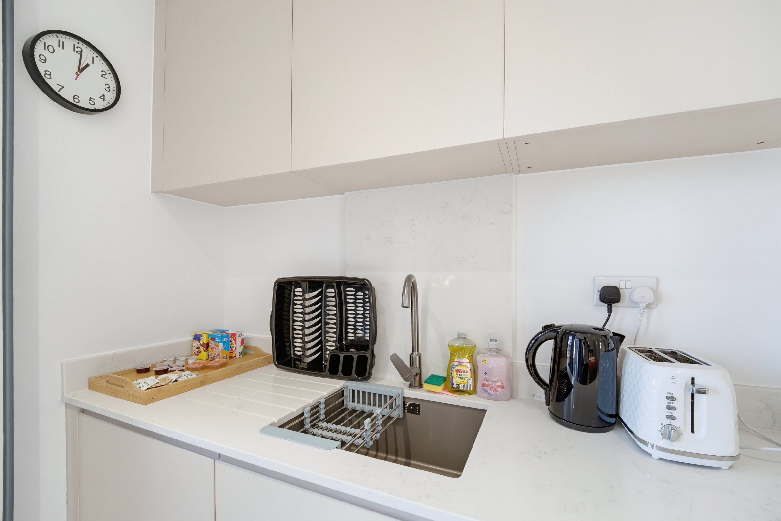 A kitchen with a sink, toaster, kettle, and a clock on the wall.