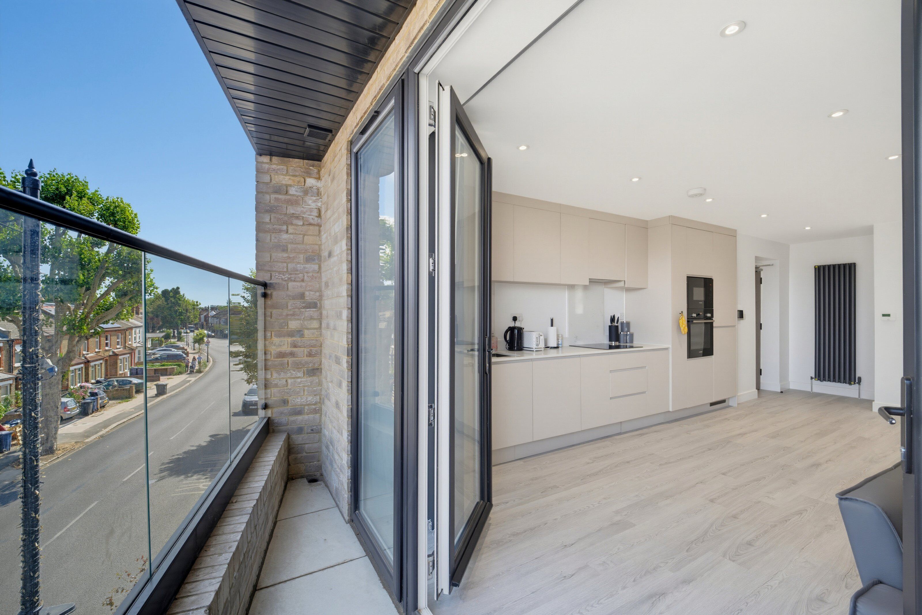 Een moderne keuken met een groot eiland, een eethoek met een tafel en stoelen, en uitzicht op de straat door een schuifdeur van glas.