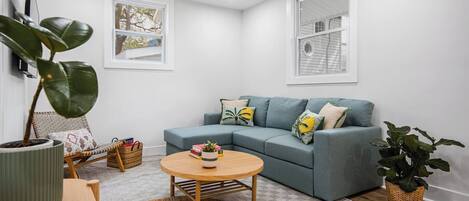 A living room with a grey sofa, a round wooden coffee table, and a large potted plant.