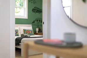 Un dormitorio con una cama, almohadas, una mesita de noche, una lámpara y una pared decorada con ilustraciones de peces.