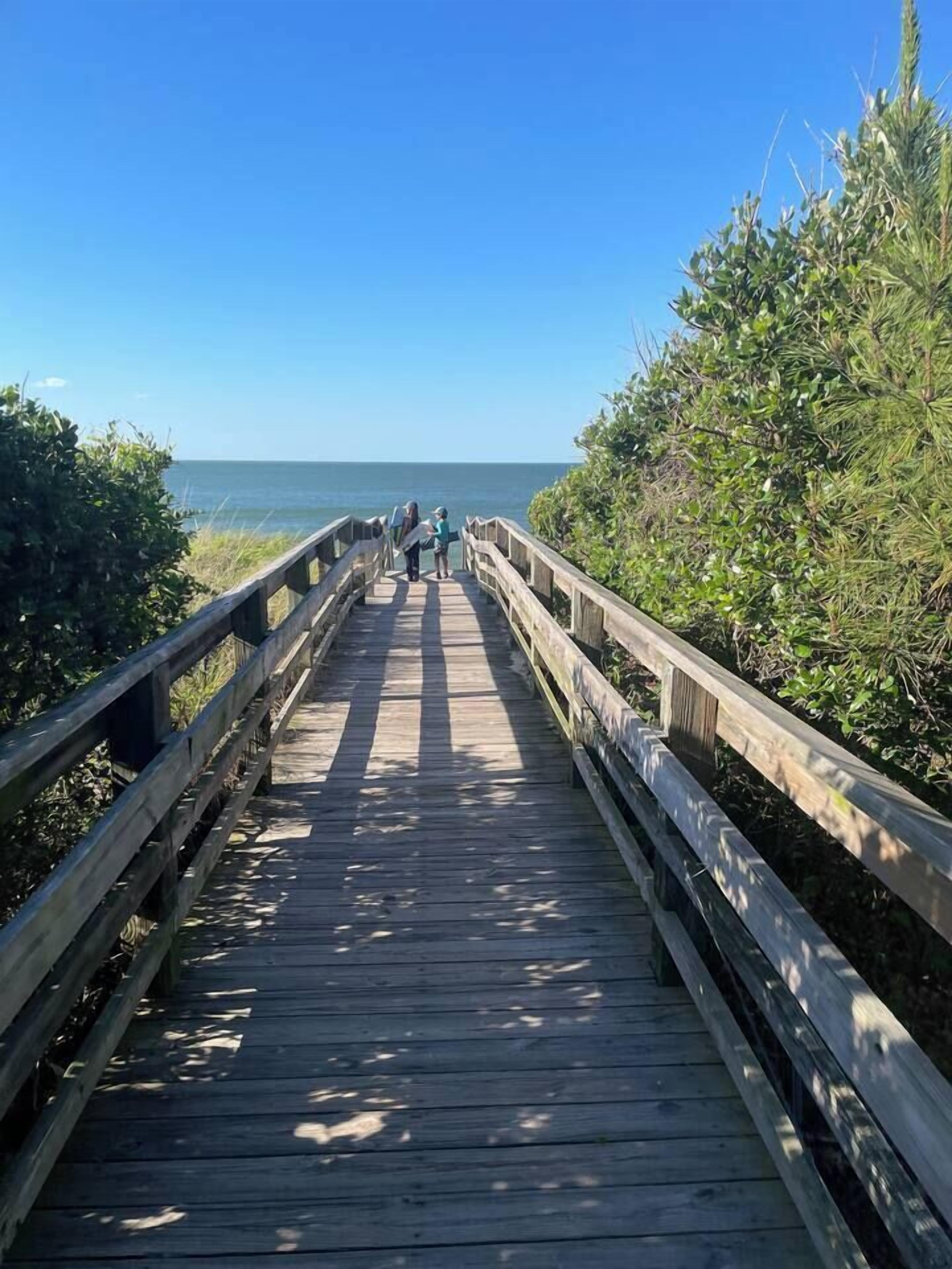 A wooden boardwalk leading to a beach with a clear sky.