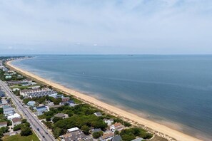 Vista aérea de una zona costera con una extensa playa de arena, una carretera paralela a la orilla y edificios residenciales.